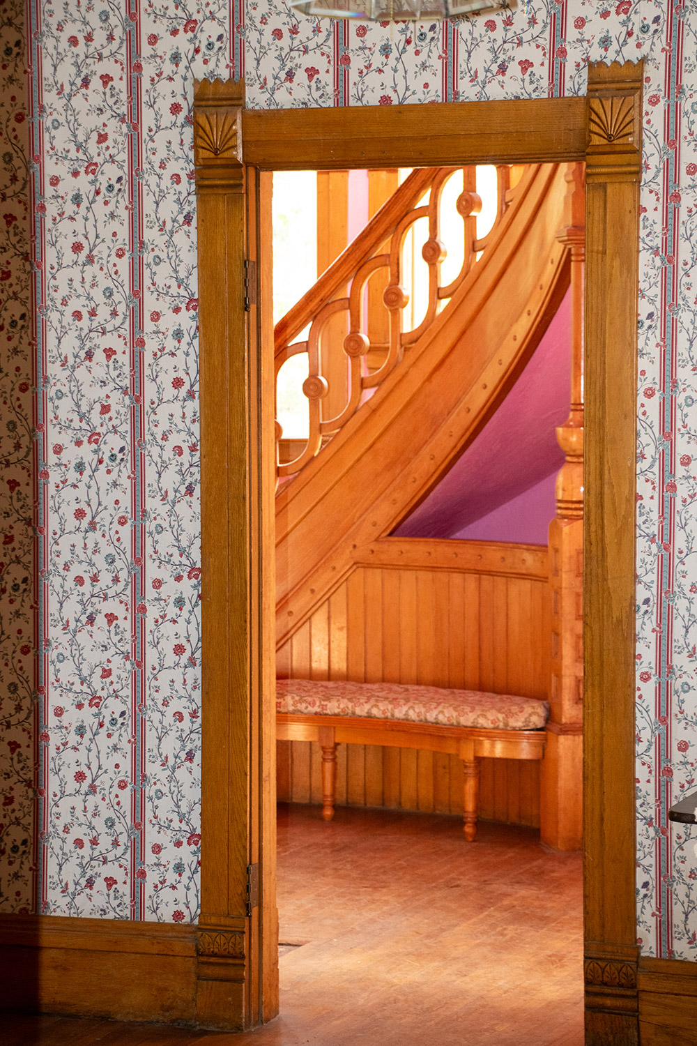 Preserving the Legacy of Colorado Cattle Country: The Castle Alonzo Hartman Built A view of the incredible wooden spiral staircase railing through a doorway in Hartman Castle, showing decorative wallpaper and intricate wood door frames.